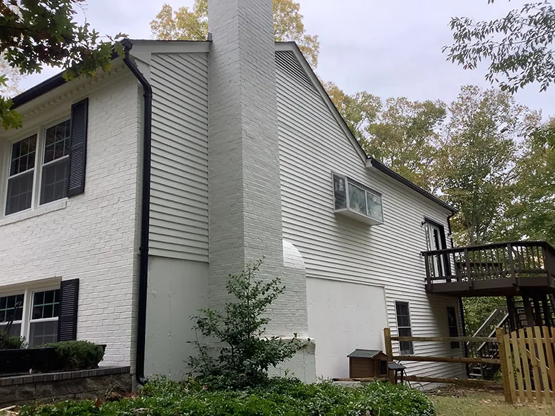 A two-story white house with a large chimney and a wooden deck surrounded by trees A two-story white house with a large chimney and a wooden deck surrounded by trees.