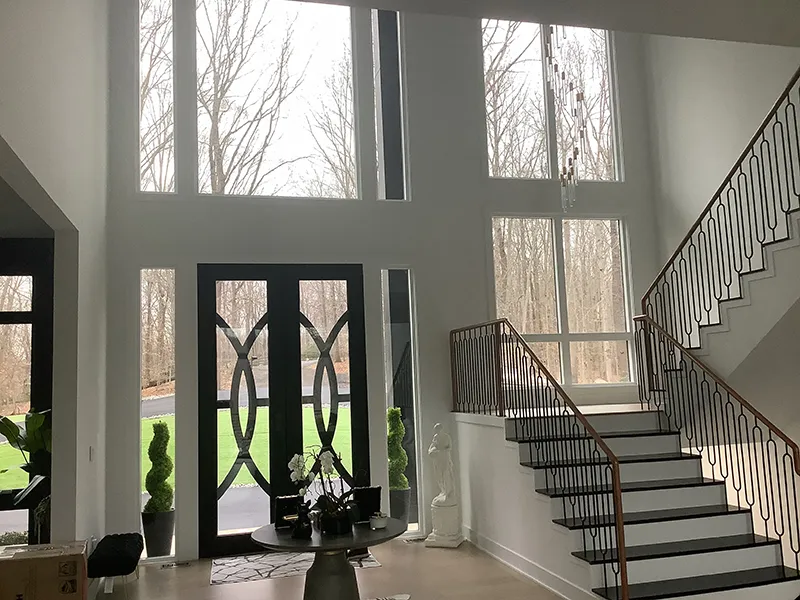 Modern foyer with tall windows, decorative door, and elegant staircase Modern foyer with tall windows, decorative door, and elegant staircase.